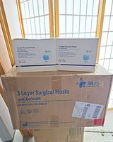 Two sealed white dispenser boxes of 3A Medical Level 3 masks on top of a larger shipping carton