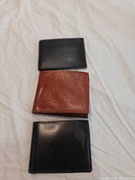 Three closed wallets, two black one brown, on white surface