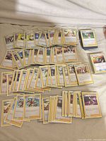 Stacks and spread of yellow-border Pokémon Trainer cards laid out on a bed