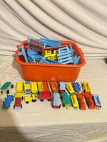 overview of orange tub with blue track pieces and multiple toy train cars laid out