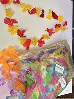 Sealed plastic bag containing multicolor leis and a few loose leis on table