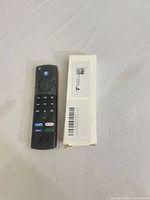 Front view of remote beside box showing controls and branded shortcut buttons