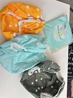 Three diaper covers in orange, mint, grey with packaging