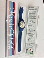 Watch in open case showing dial, strap and instructions