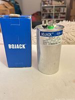 Front view of Bojack CBB65B capacitor beside original box