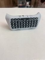 Front view of light gray wireless mini QWERTY keyboard showing black keys and navigation buttons