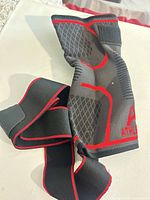 Front view of grey/black knee sleeve showing red edging and attached strap