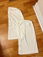 Two off-white pillowcases laid flat on wood floor showing overall size and color