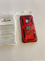 Front view of red rugged case in plastic next to sealed instructions pouch
