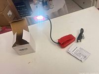Light assembled with red LED illuminated, box, cable and instruction sheet visible