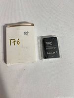 Battery in plastic sleeve beside plain white box