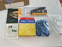 All items laid out: crimper, stripper, cable tester box, bag of blue boots, bag of clear connectors, pamphlet