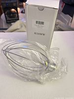 Wire whip in plastic wrap beside box showing model number
