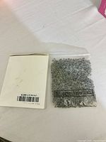 Bag of translucent gray alphabet beads alongside outer white cardboard sleeve