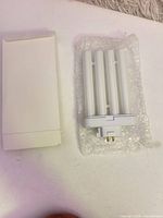Bulb in bubble wrap beside white box, showing 2-pin base and four tubes