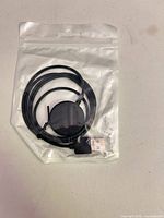 Front view sealed clear pouch showing black magnetic charging pad and USB-A plug