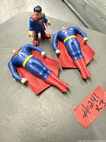 Three Superman figures on table, two large lying, one small standing