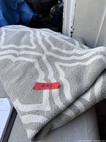 Folded grey and off-white geometric patterned rug with red inventory sticker #203 visible