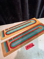 Two rectangular multicolor wooden cribbage boards displayed on table