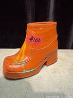 Front view of orange metal boot coin bank showing overall form and paint wear