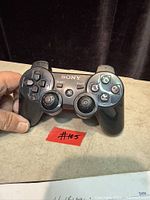 Front view of black Sony DualShock 3 controller showing buttons and worn thumbsticks