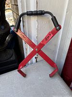 Front view of red metal X-clamp battery carrier with black handle