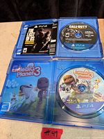 Open PS4 game cases for The Last of Us Remastered and LittleBigPlanet 3 with discs visible, plus loose Call of Duty PS4 disc
