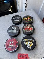 Top view of six hockey pucks laid out showing all printed logos