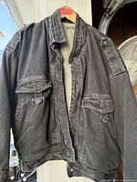 Front view of black denim jacket on hanger showing pockets, collar, label and overall condition