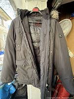 Full view of black Canadiana parka on hanger showing hood, pockets, front closure
