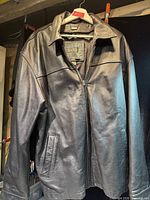 Front view of black leather jacket on hanger showing zipper and pockets