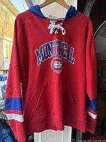 Front view of red Champion Montreal Canadiens lace-up hoodie displaying graphics, pocket, sleeve stripes