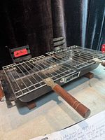 Overall view of portable hibachi grill showing grate, body, wooden handles and vent