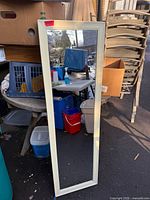 Full view of rectangular wall mirror with white wood frame leaning outdoors