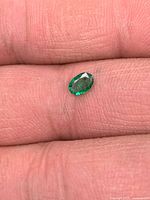 Small oval green emerald shown on fingertip for scale