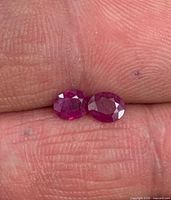 Two oval rubies resting on fingertip