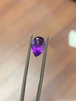Pear-shape purple amethyst held by tweezers
