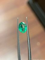 Emerald held by tweezers showing oval cut and colour
