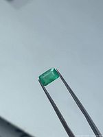 Rectangular green emerald held in tweezers