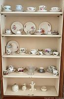 Full cabinet view showing assorted teacups, saucers, plates and figurines