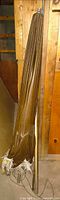 Folded brown canopy with white fringe attached to metal pole leaning against wall