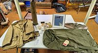 Overall view of jacket, shell casing, plaque, duffel, manuals and small items on table