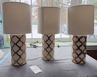 Front view of three matching ceramic table lamps with shades on tabletop