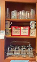 Cabinet view showing tall glasses, boxed Lenox bowls, boxed collector mugs, mugs, and tumblers in caddy