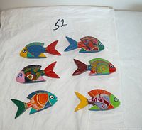 All six multicolored hand painted wooden fish displayed on cloth