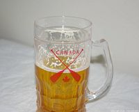 Front view of clear glass mug with CANADA paddles logo, partial beer shown