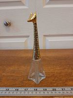 Full view of bottle showing glass body and metal giraffe neck and head, ruler for scale