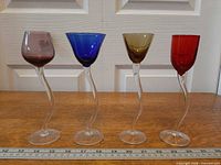 Front view of four colored bowl liqueur glasses with ruler