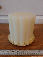 Side view of ivory fluted pillar candle on gold riser with ruler for scale