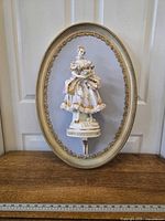 Full view of framed porcelain figurine wall hanging with ruler for scale
